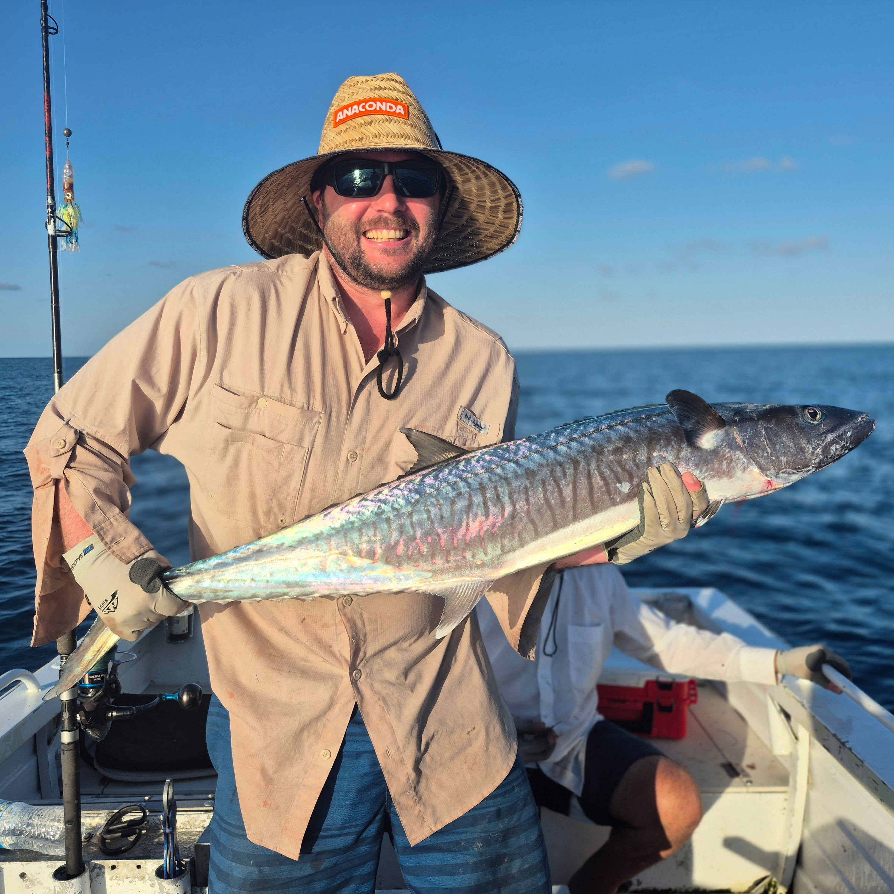 Man holding a large fish on a boat with a clear blue sky and ocean background